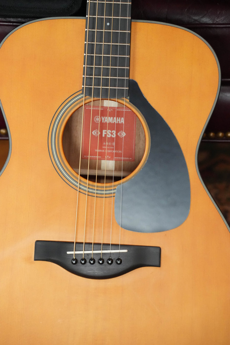 Close-up of the Yamaha FS3 Red Label Concert Acoustic Guitar #1516 by Yamaha, highlighting its solid Sitka spruce top, black pickguard, strings, bridge, soundhole with red label, and natural wood finish on a smaller concert body.