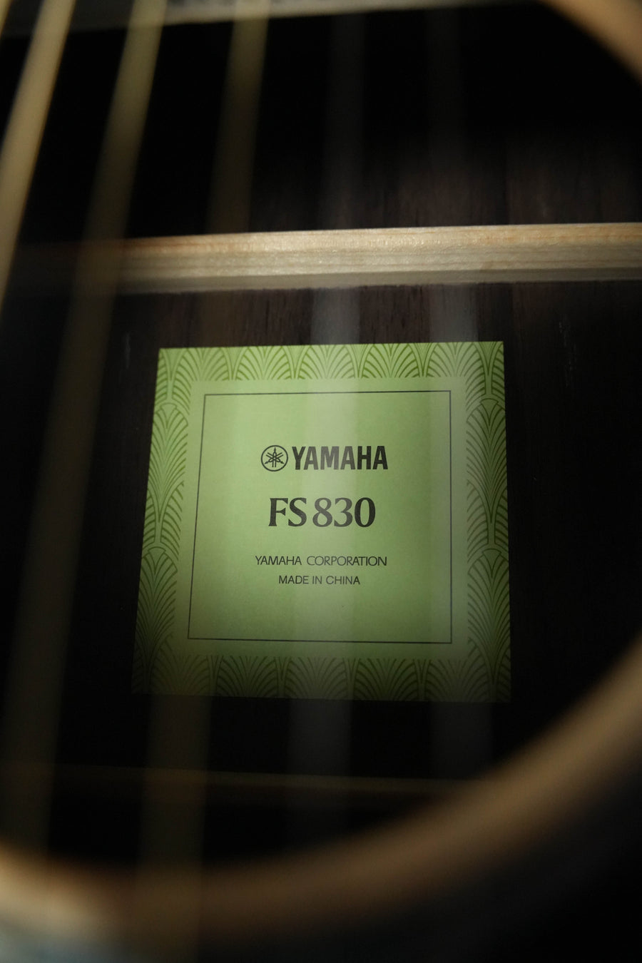 Close-up through guitar strings shows a green label inside a Yamaha FS830 Concert Acoustic Guitar #1751 by Yamaha, with a solid spruce top. The label reads: Yamaha FS830, Yamaha Corporation, Made in China.
