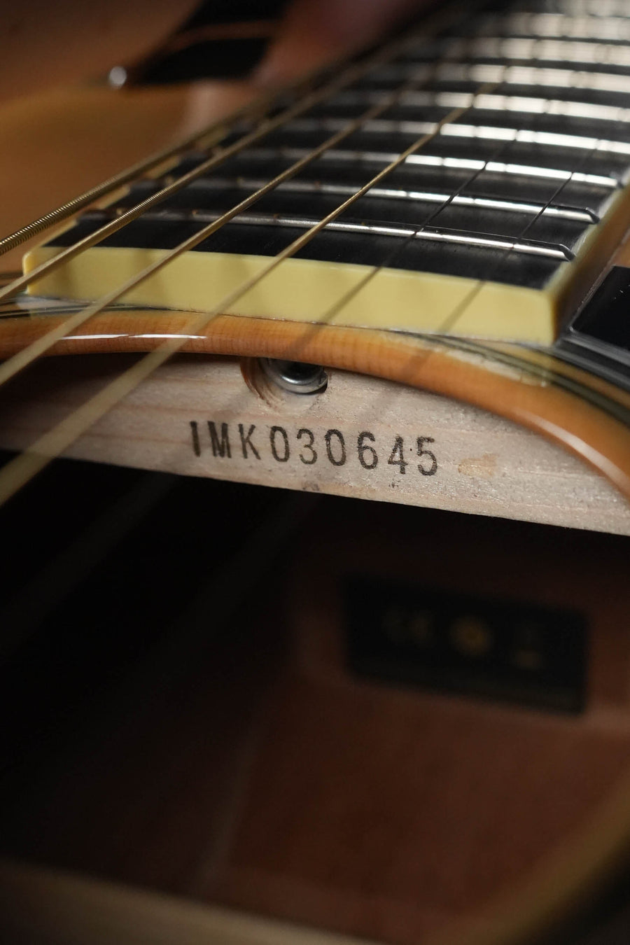 Close-up of the inside of a Yamaha LL16M ARE Engelmann/Mahogany Original Jumbo Acoustic Guitar w/ SRT Zero Impact Pickup (#0645) by Yamaha, highlighting the serial number IMK030645 stamped below the strings and fretboard.