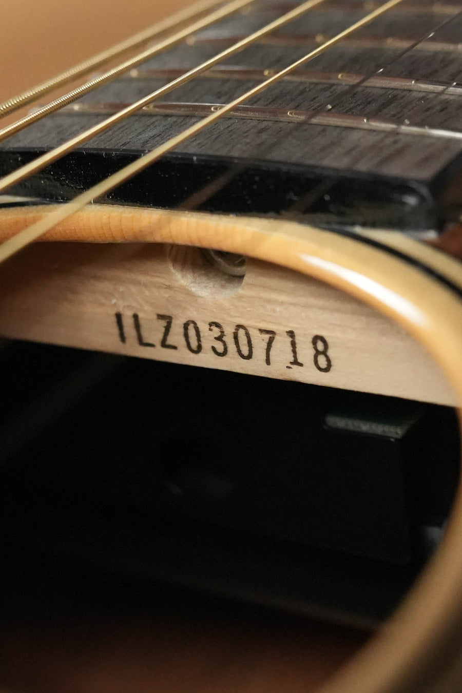 Close-up of a Yamaha TAG1 C Natural Finish Dreadnought Cutaway Acoustic-Electric Guitar’s sound hole and strings, showing serial number #0718 printed on the wooden interior bracing.
