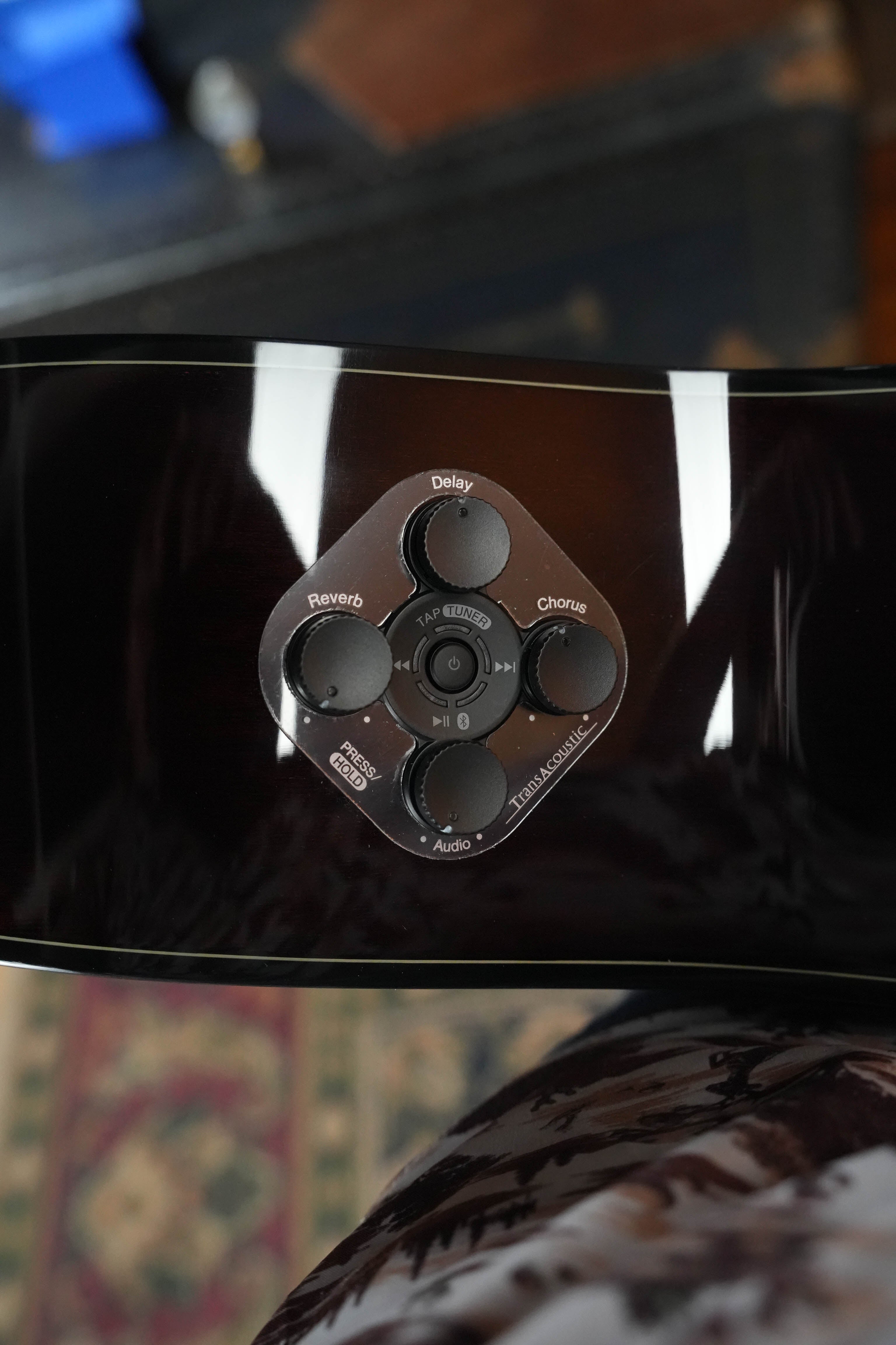 Close-up of the control panel on a Yamaha TAG1 C Natural Finish Dreadnought Cutaway Acoustic-Electric Guitar, featuring buttons for Reverb, Delay, Chorus, Tap/Enhance, and Audio with reflections and part of a patterned rug visible.