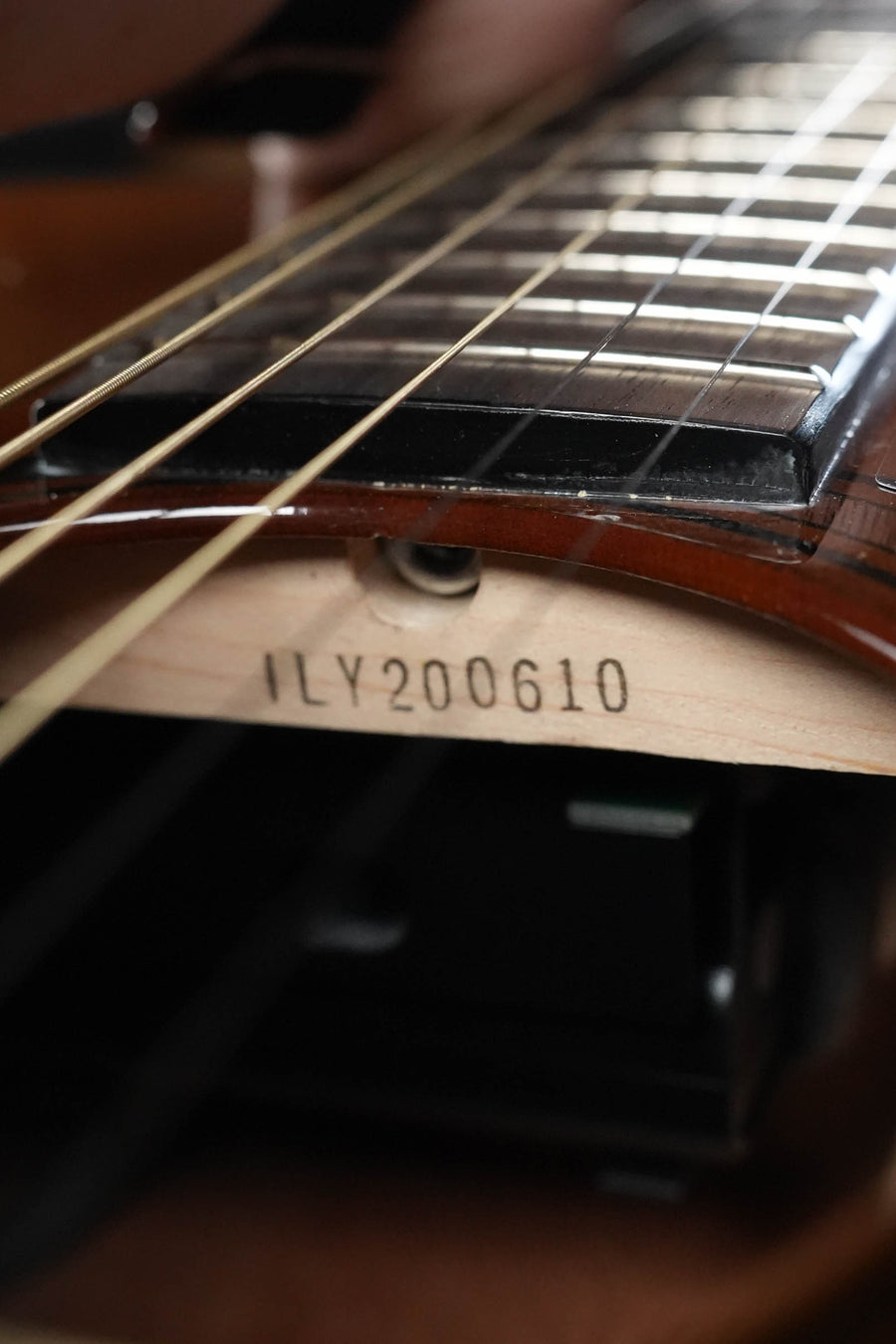 Close-up of a Yamaha TAG1 C Sitka/Mahogany Sandburst Dreadnought Transacoustic Guitar w/Cutaway #0610’s neck and strings, featuring its innovative TransAcoustic system and serial number #0610 on the wood beneath.