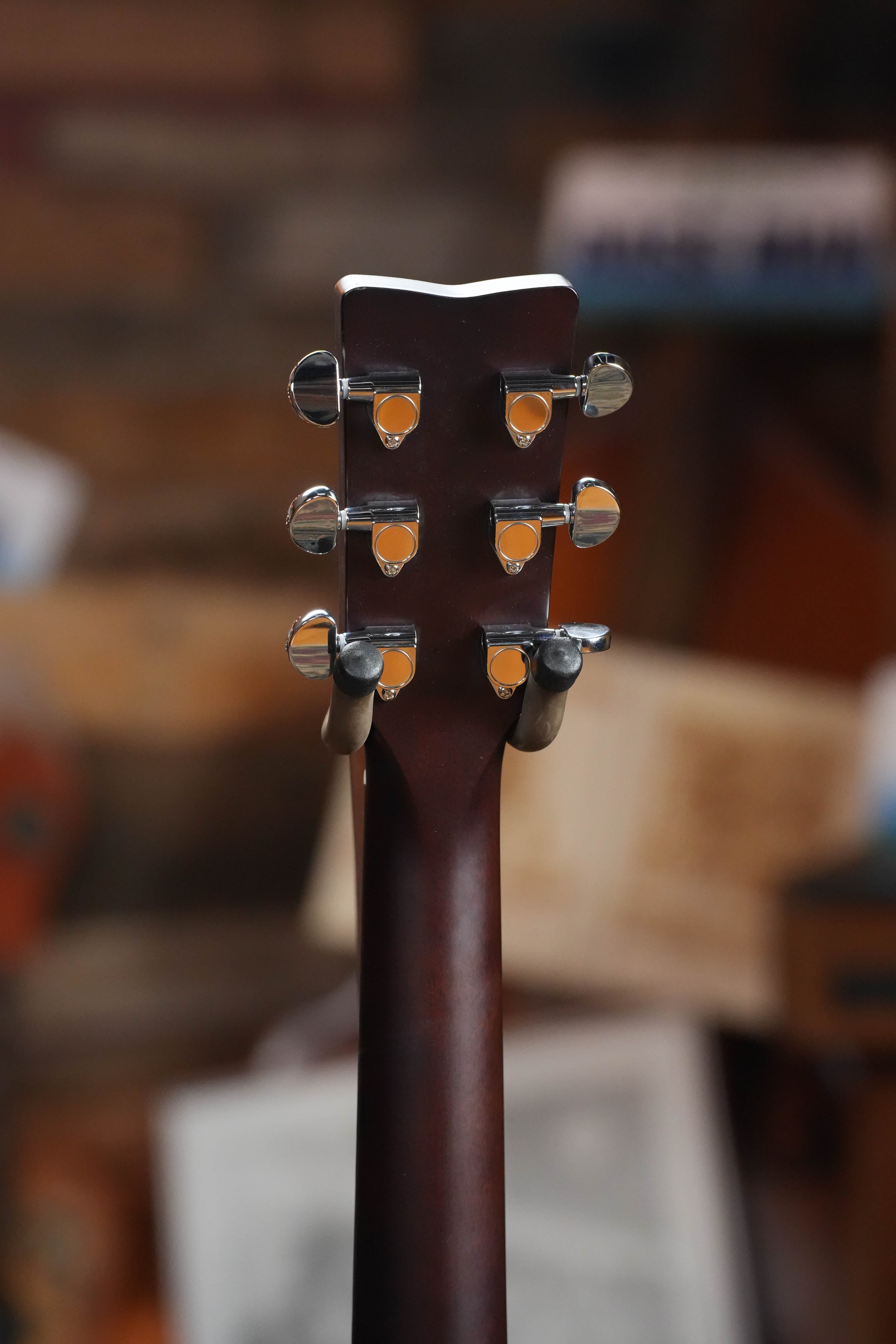 Close-up of the Yamaha TAG1E TBL Spruce/Mahogany Transacoustic Dreadnought Guitar #1280 headstock with six tuning pegs, set against a blurred background with musical and wooden elements.
