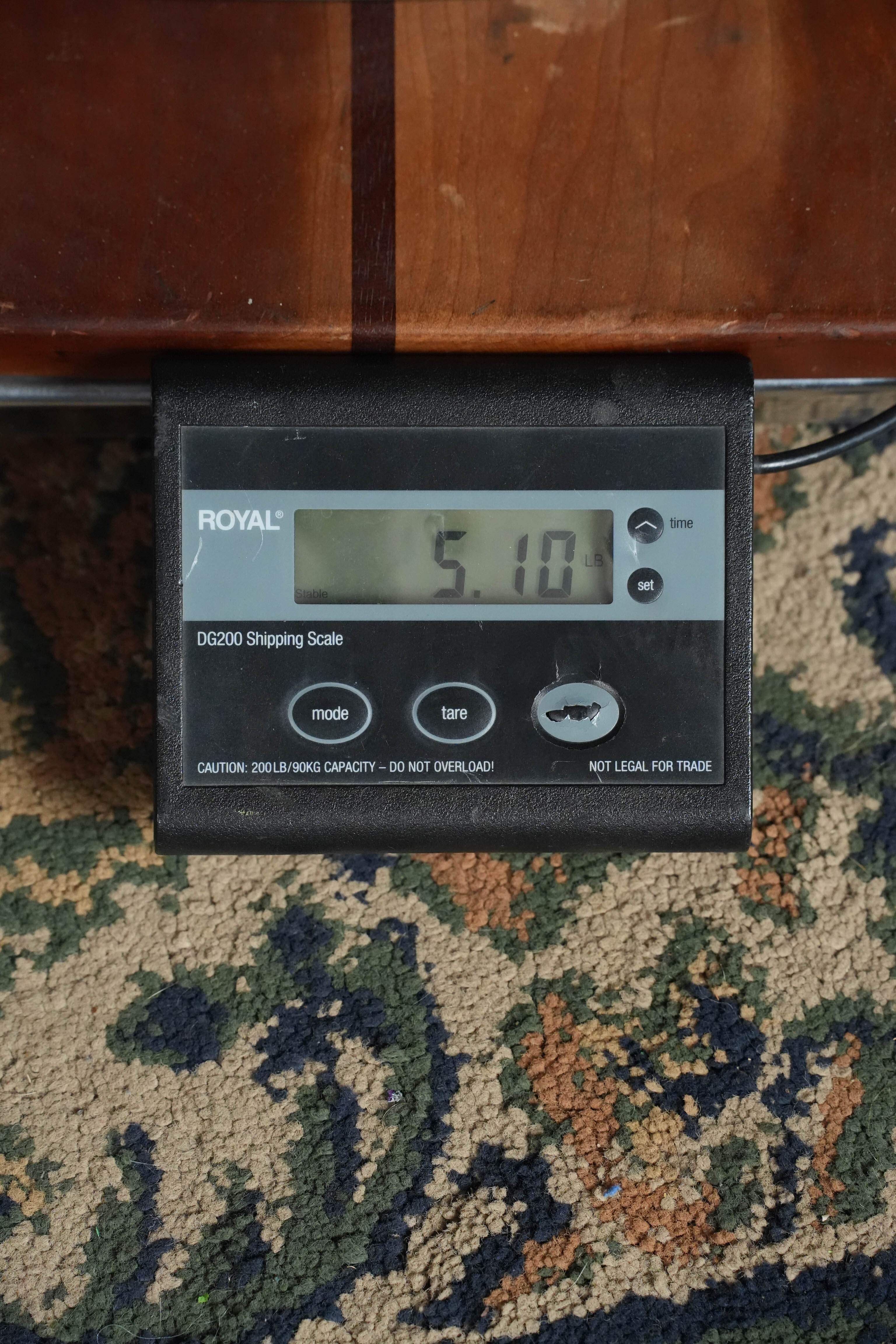 A digital shipping scale on a patterned carpet shows 5.10 pounds beneath a wooden surface—much like weighing the Yamaha TAG1E TBL Spruce/Mahogany Transacoustic Dreadnought Guitar #1280 by Yamaha with built-in reverb and chorus effects.