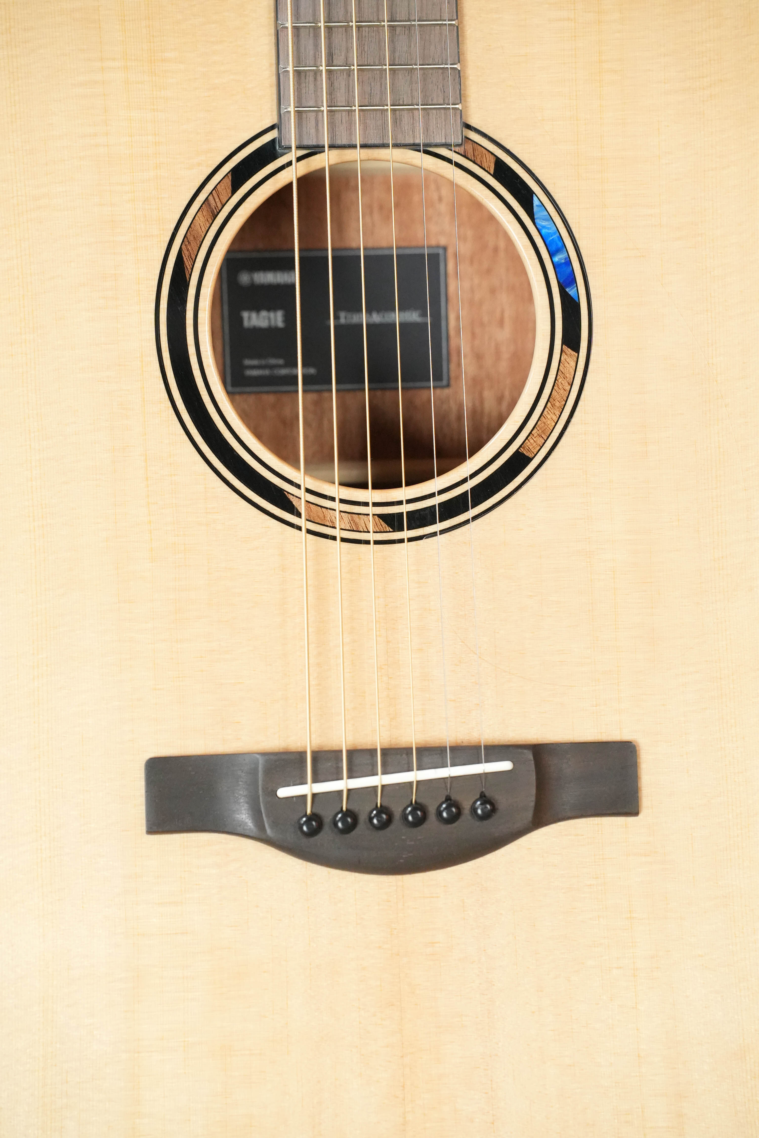 Close-up of the Yamaha TAS1E Natural Finish Concert Acoustic-Electric Guitar #1133 by Yamaha, showing its solid spruce top, mahogany back and sides, sound hole, strings, bridge, fretboard, and visible Yamaha label.
