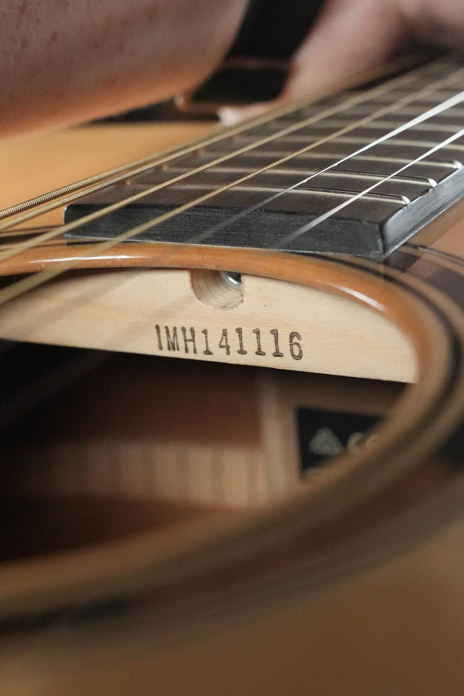 Close-up of a person’s hand playing a Yamaha TAG1E TransAcoustic Natural Finish Dreadnought Acoustic-Electric Guitar (#1116), focusing on the soundhole where the model number is visible on the inner wood brace.