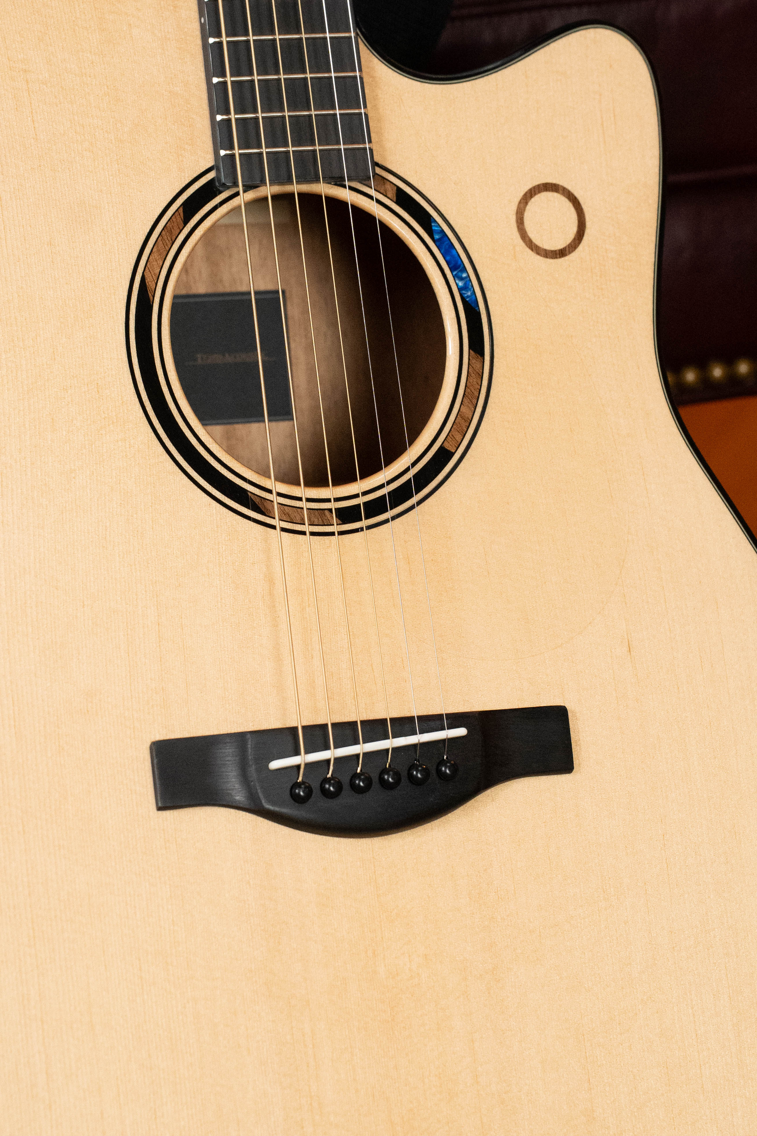 Close-up of the Yamaha TAG3C-NT Sitka/Mahogany Natural Dreadnought Guitar body, showing six strings, sound hole, bridge, and fretboard. This Yamaha features a cutaway design and the newest TransAcoustic System.