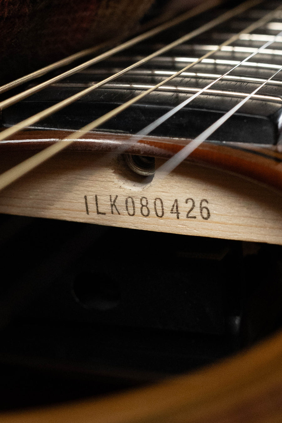 Close-up of a Yamaha TAG3C-SDB Sandburst Dreadnought Guitar’s interior, displaying metal strings and serial “#0426” stamped on a brace inside this Sitka/Mahogany guitar with the newest TransAcoustic System.