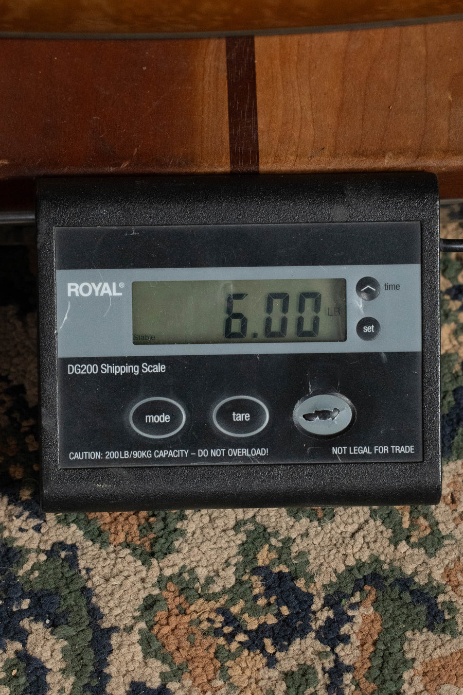A ROYAL DG200 Shipping Scale on a patterned carpet displays 6.00 pounds, possibly weighing a Yamaha TAG3C-SDB Sitka/Mahogany Sandburst Dreadnought Guitar with the NEWEST TransAcoustic System #0426 by Yamaha. Several buttons and warnings are visible on the scale.