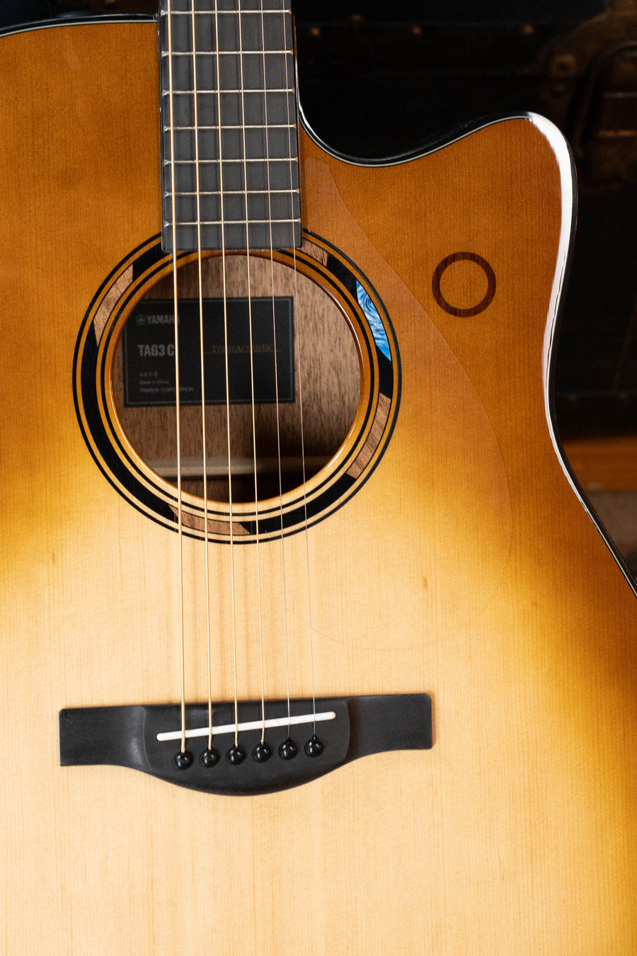 Close-up of the Yamaha TAG3C-SDB Sitka/Mahogany Sandburst Dreadnought Guitar, highlighting its soundhole, strings, wood grain, and the NEWEST TransAcoustic System #0592.