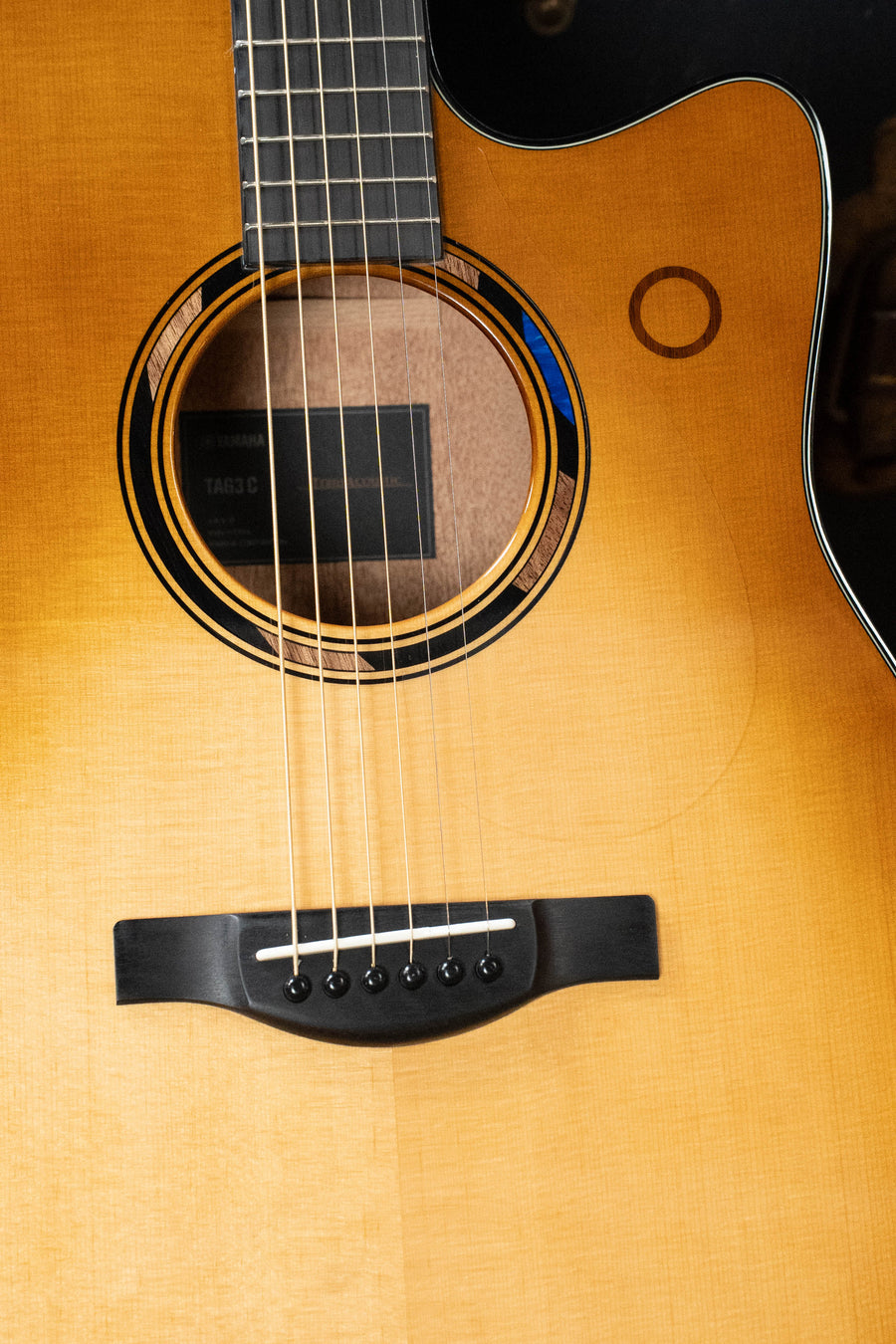 Close-up of the Yamaha TAG3C-SDB Sitka/Mahogany Sandburst Dreadnought Guitar with the NEWEST TransAcoustic System #0760, highlighting strings, bridge, sound hole, and part of the neck.