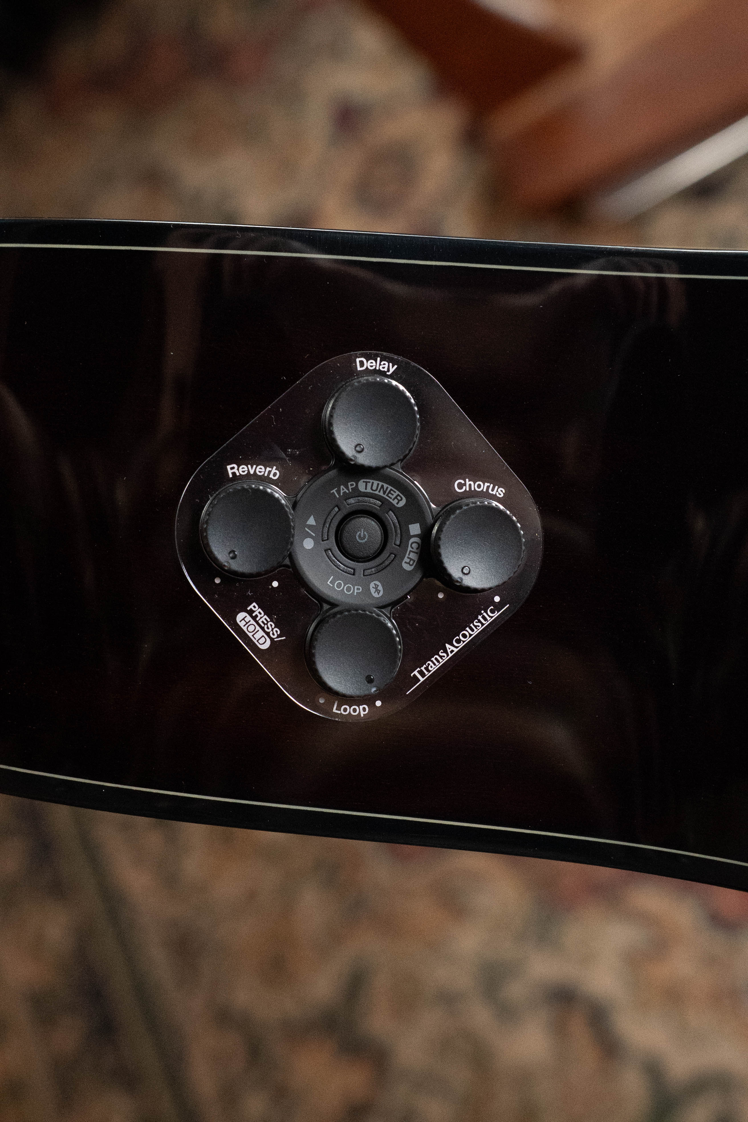 Close-up of the Yamaha TAG3C-SDB Sitka/Mahogany Sandburst Dreadnought Guitar’s effects panel, showing Delay, Chorus, Reverb, Loop, Tap Button controls and its newest TransAcoustic System by Yamaha set against a blurred background.