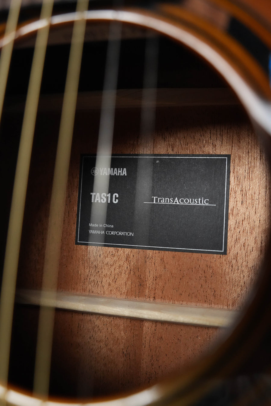 Close-up of a Yamaha TAS1 C Sitka/Mahogany Sand Burst Transacoustic Concert Guitar’s soundhole with cutaway, showing the inside label, Sitka spruce wood grain, and guitar strings in the foreground.