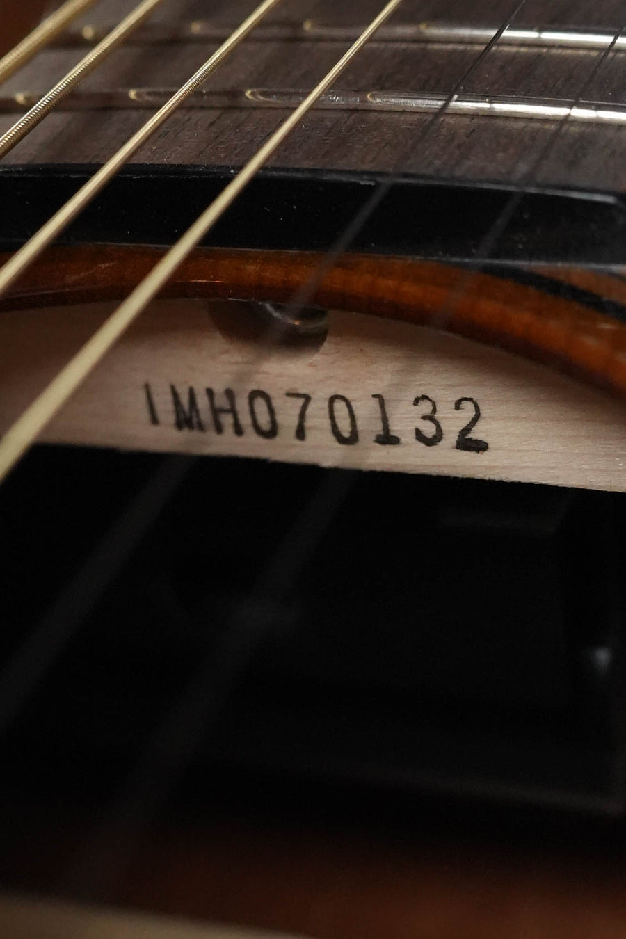Close-up of the Yamaha TAS1 C Sitka/Mahogany Sand Burst Transacoustic Concert Guitar with Cutaway (#0132) serial number, seen inside the body through the strings and sound hole, highlighting fretboard and Sitka spruce top grain.