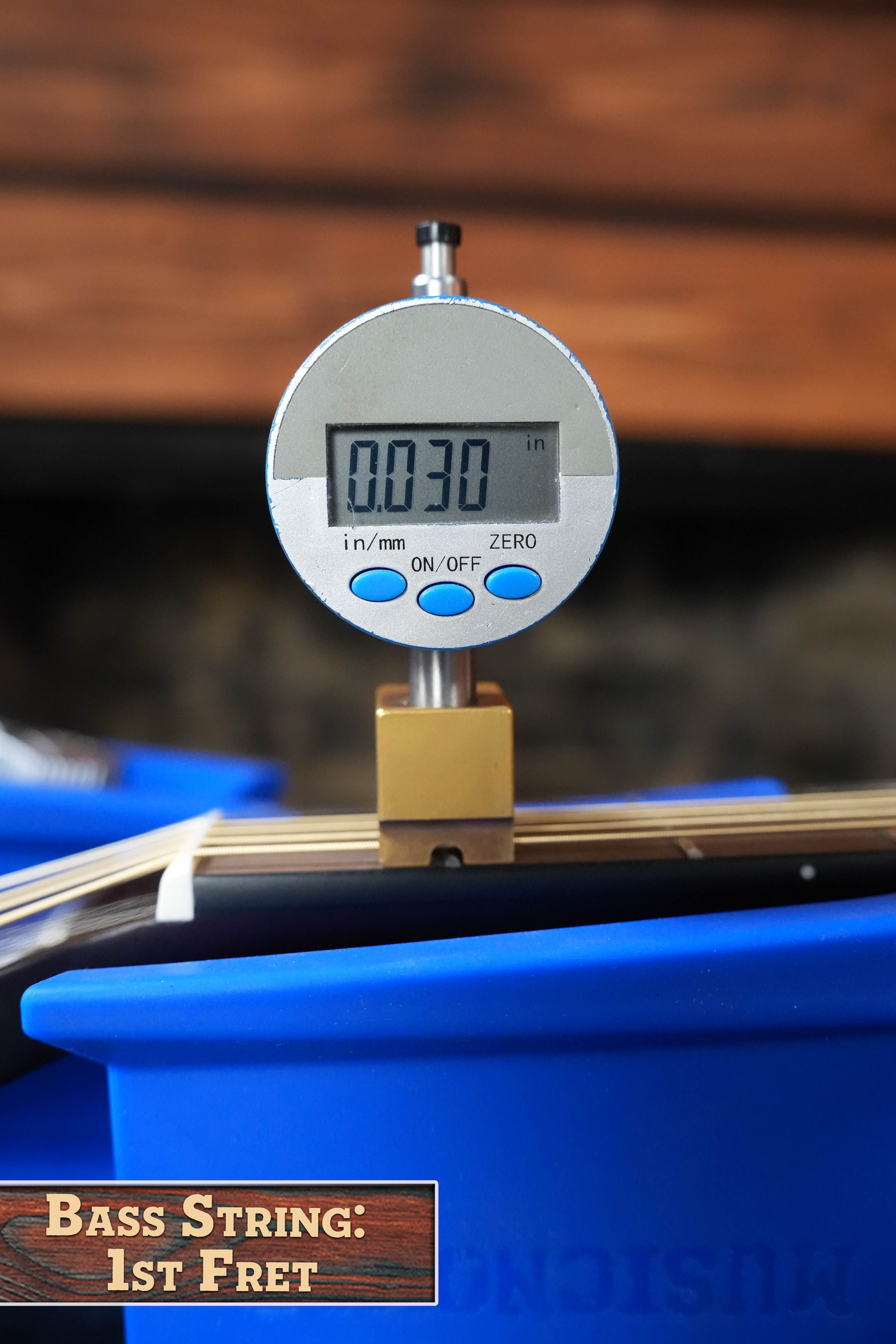 A Yamaha TAS1 C Sitka/Mahogany Sand Burst Transacoustic Concert Guitar w/Cutaway #0132 rests on a blue support as a digital caliper displays the bass string height at the 1st fret: 0.030 inches. Label: Bass String: 1st Fret.