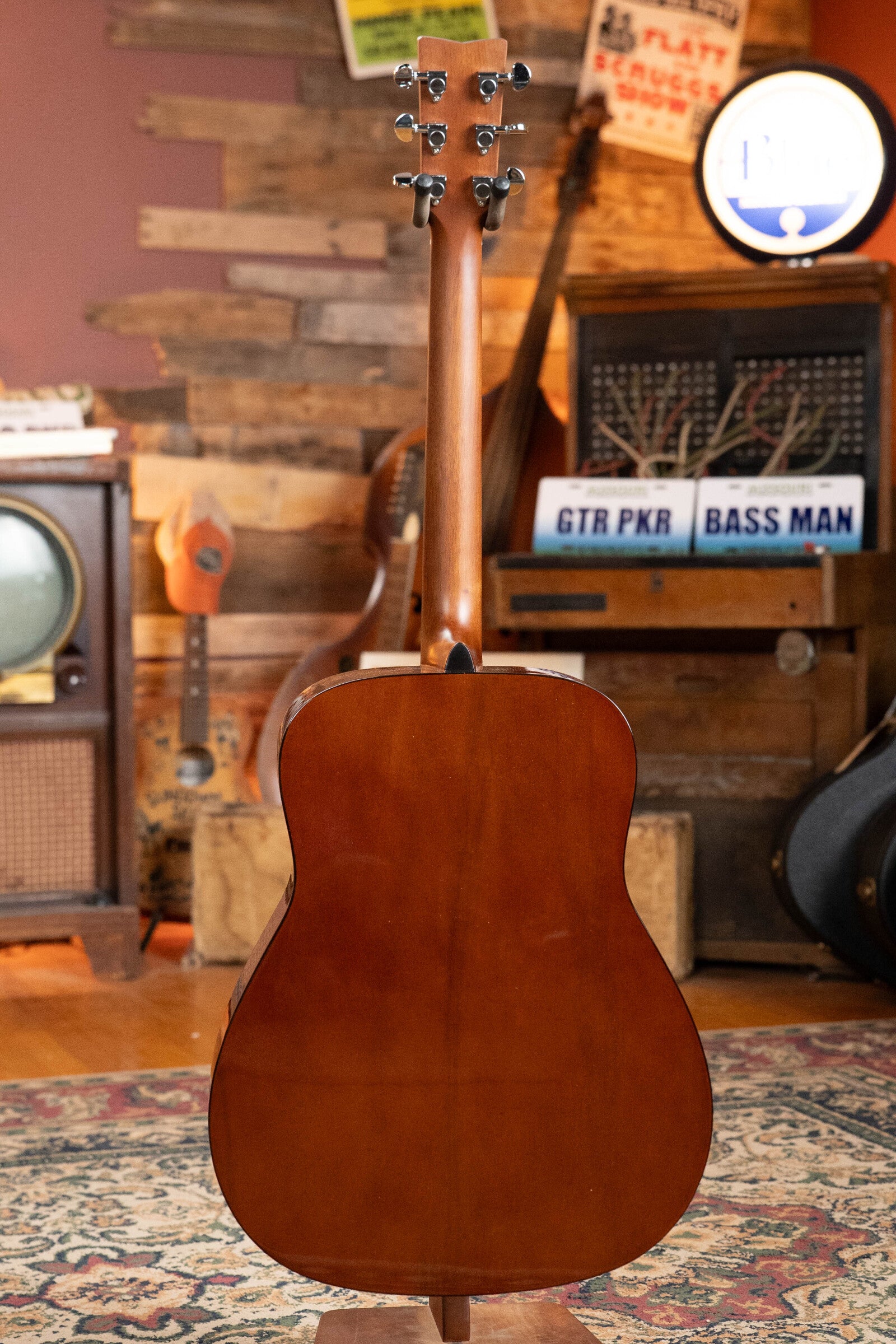 The image features the Yamaha GigMaker Deluxe Acoustic Pack - Natural Finish #8229 by Yamaha, displayed upright on a patterned rug with vintage music gear and wooden decor—ideal inspiration for an acoustic guitar starter setup.